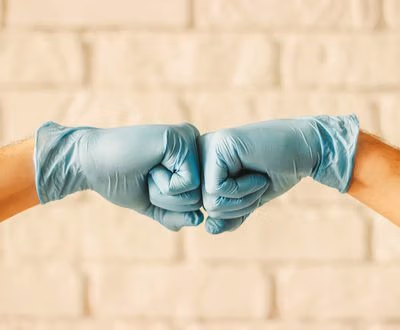 Two,Men,Bumping,Hands,In,Blue,Medical,Gloves,As,Protection