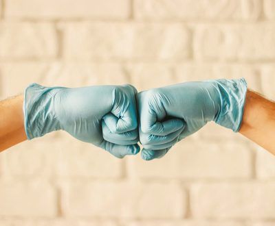 Two,Men,Bumping,Hands,In,Blue,Medical,Gloves,As,Protection