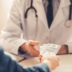 Cropped,Image,Of,Young,Doctor,In,White,Coat,Talking,Money